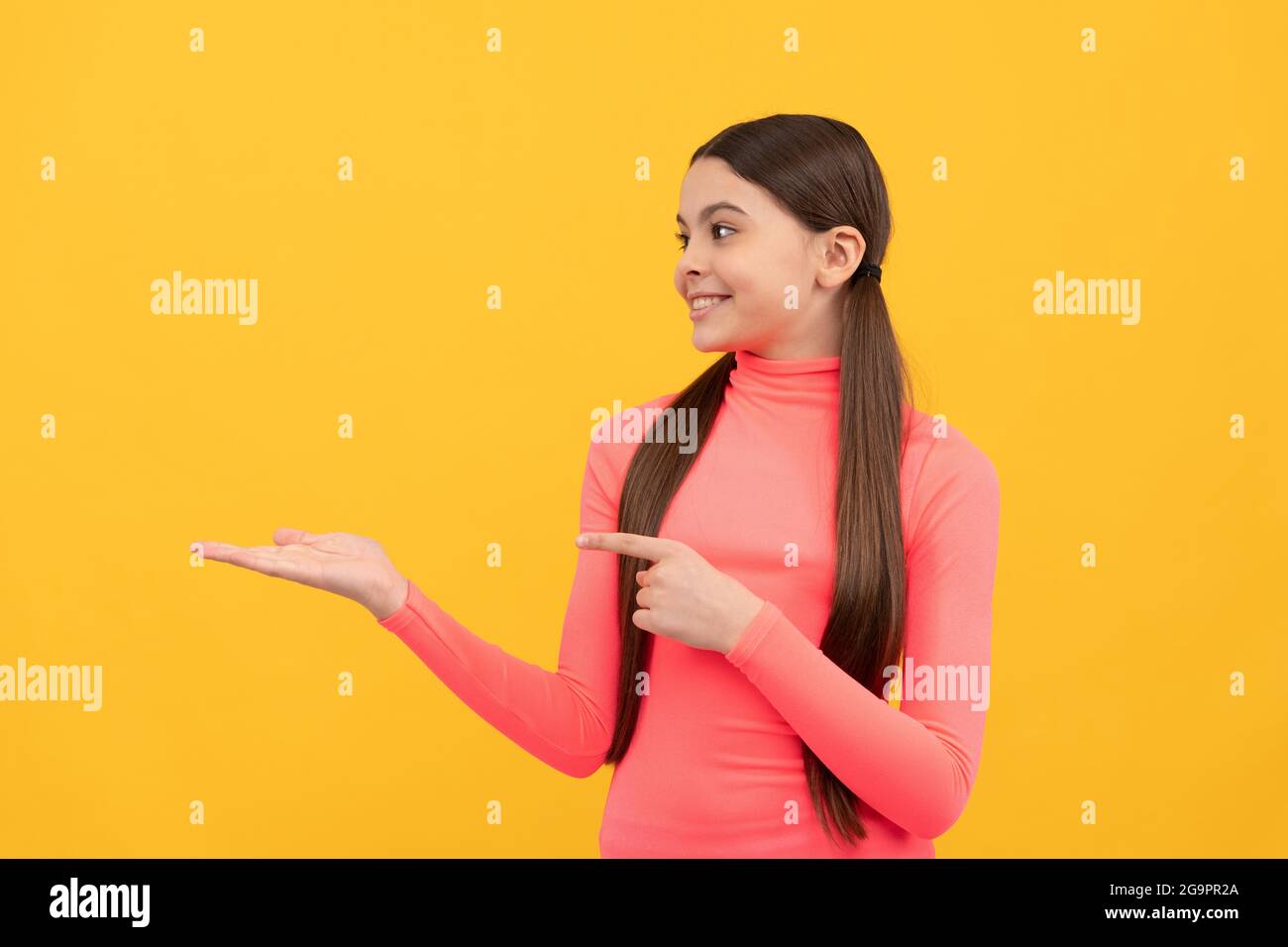 Glückliches Kind zeigt Finger auf Kopierplatz auf gelbem Hintergrund, Angebot Stockfoto