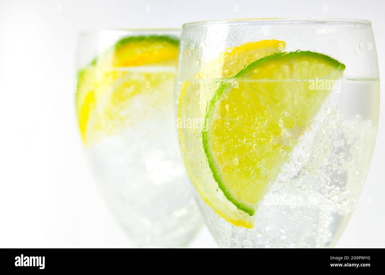 Zwei stielige Gläser mit sprudelndem Eiswasser und Zitronen- und Limettenscheiben auf Weiß Stockfoto