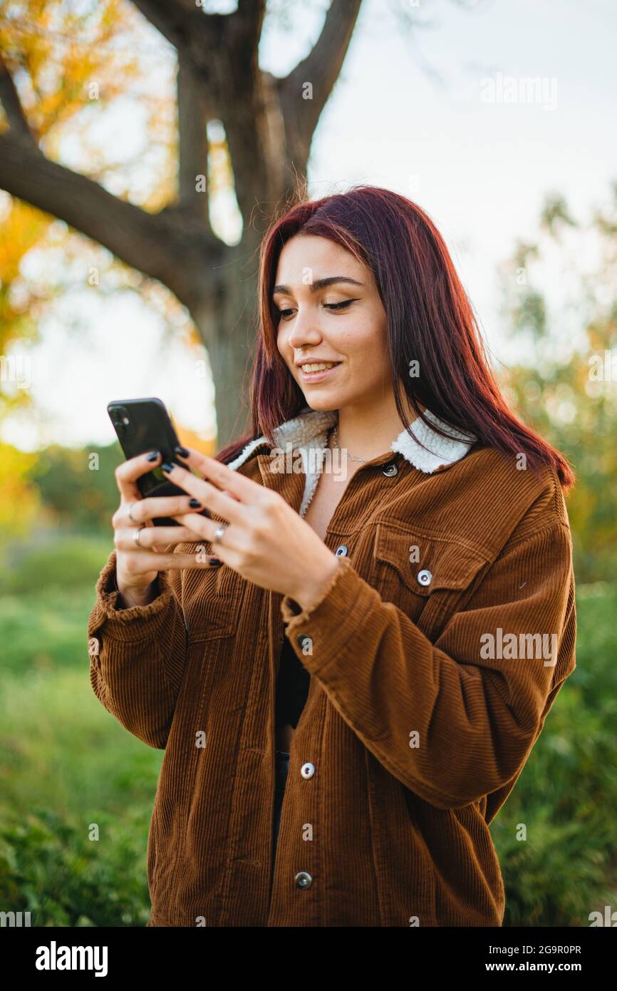 Glückliches Teenager-Mädchen zu Fuß, während sie ihr Telefon verwenden, um eine Nachricht zu schreiben. Sie chattet online mit Freunden. Stockfoto