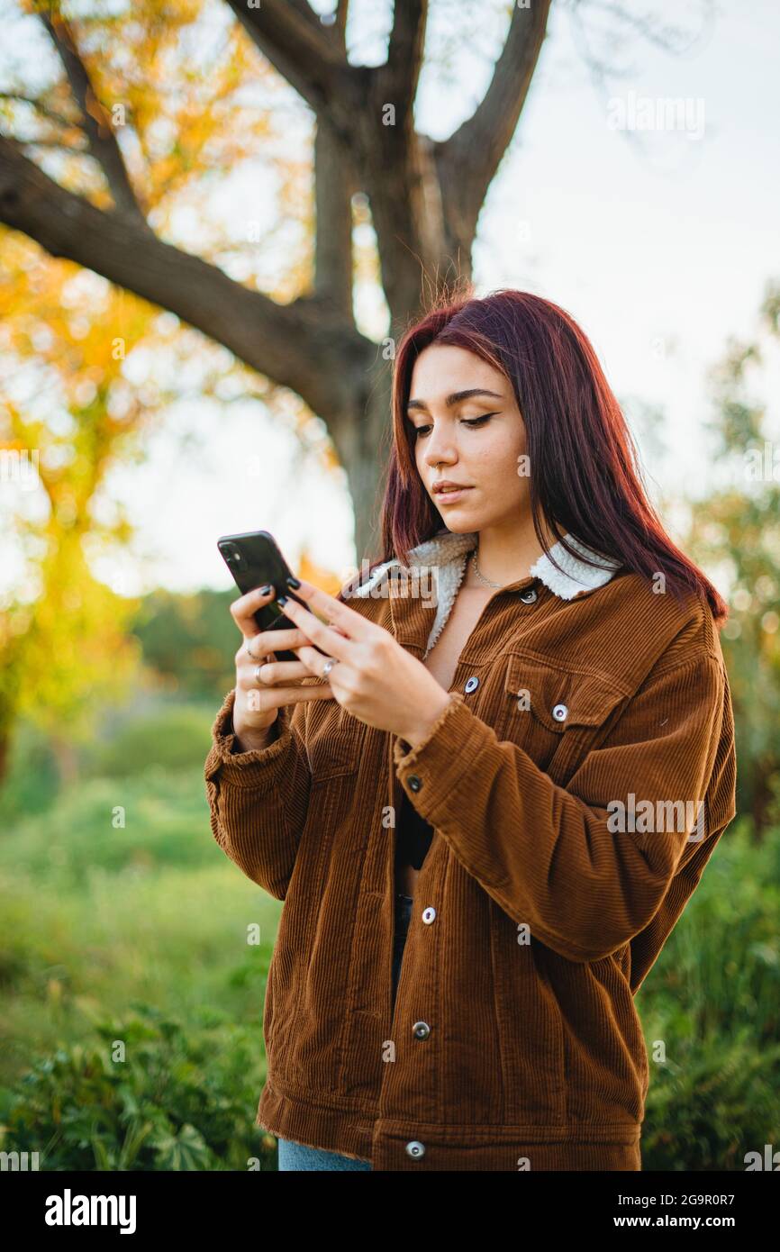 Teenager-Mädchen, das ihr Telefon benutzt, um eine Nachricht zu schreiben, während sie auf dem Feld spazieren geht. Sie chattet online mit Freunden. Stockfoto