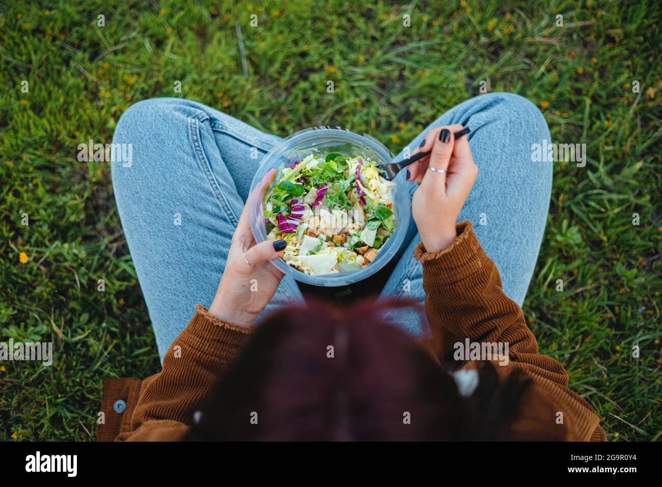 Teenager Mädchen essen einen Salat, während sie auf Gras sitzen. Sie genießt die Ruhe. Von oben aufgenommen. Stockfoto