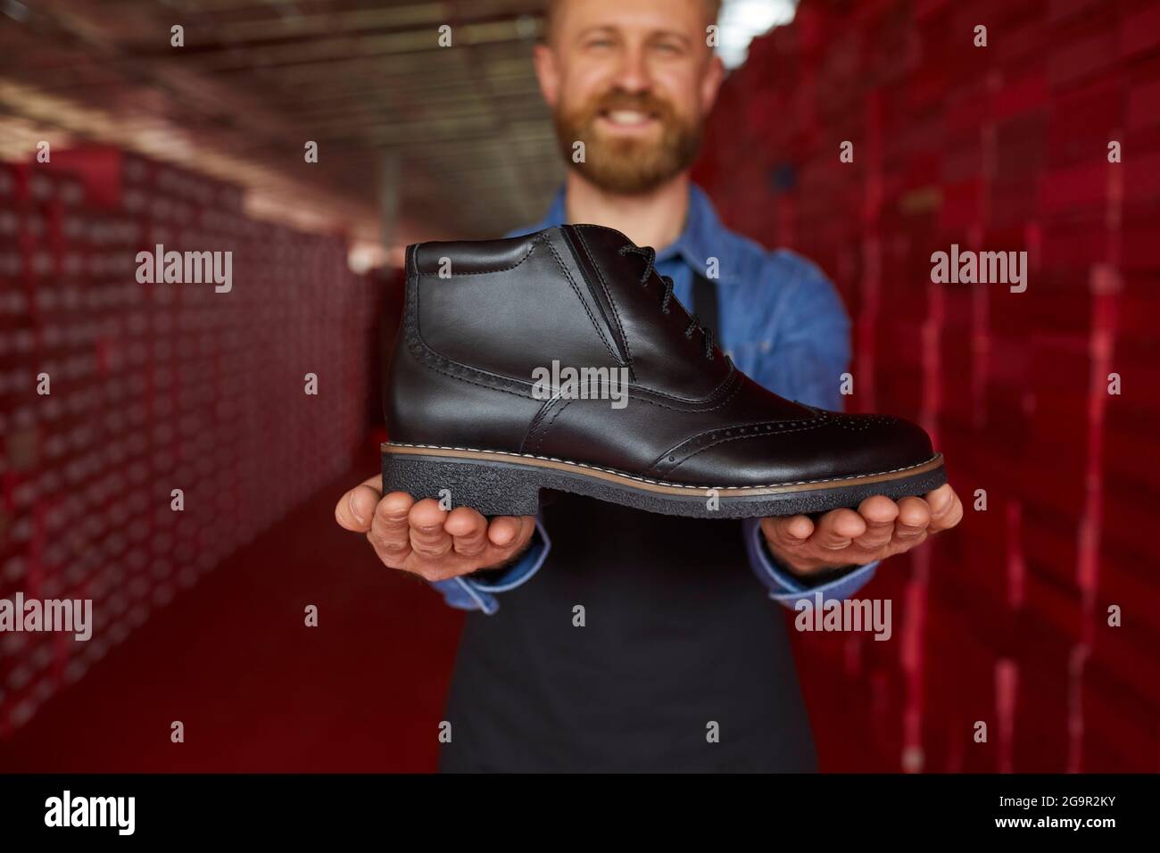 Glücklicher Lagerarbeiter oder Besitzer einer Schuhfabrik, der einen neuen schwarzen Lederstiefel zeigt Stockfoto
