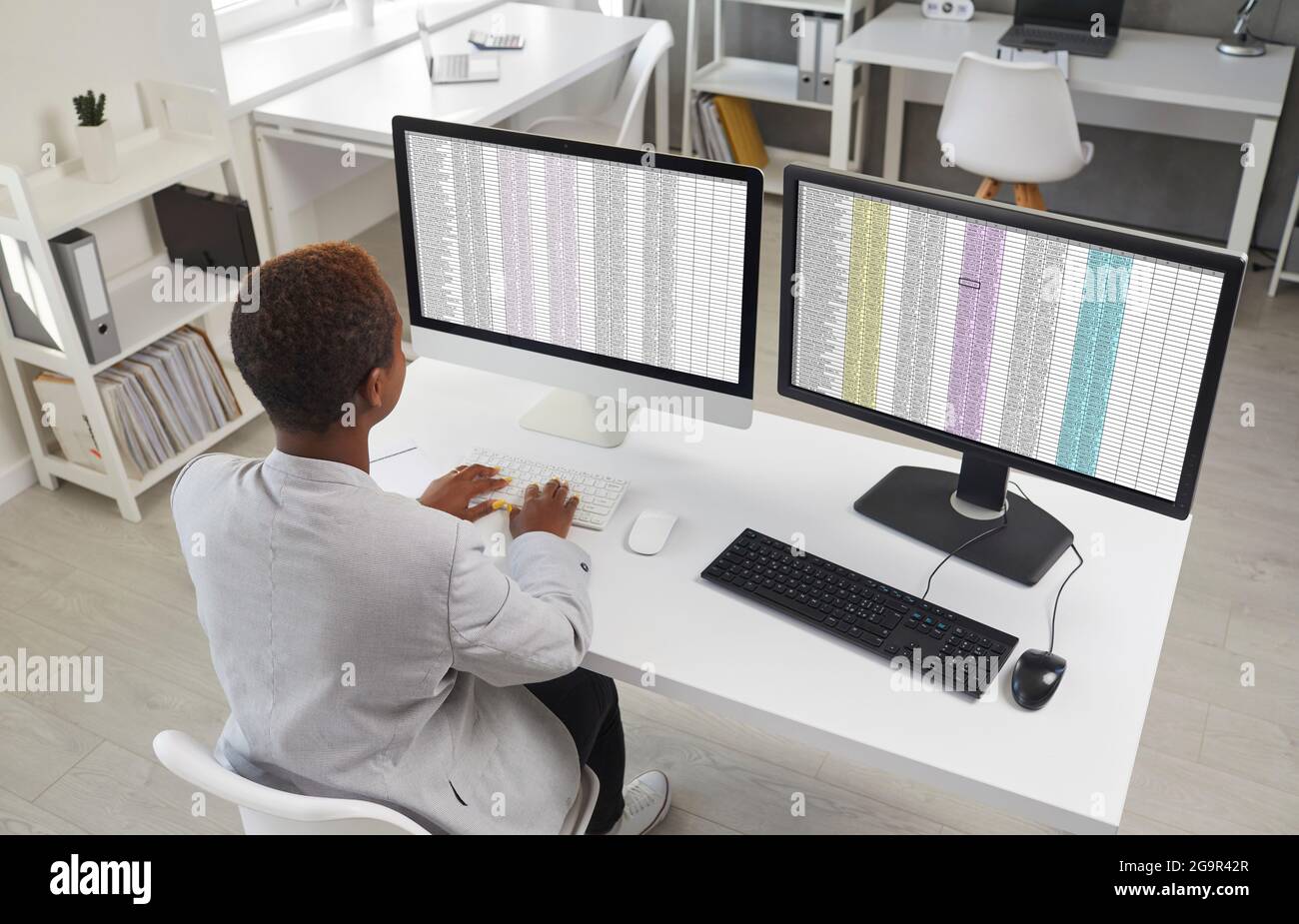 Finanzbuchhalter sitzt am Schreibtisch und arbeitet mit Tabellenkalkulationen auf zwei Desktop-Computern Stockfoto
