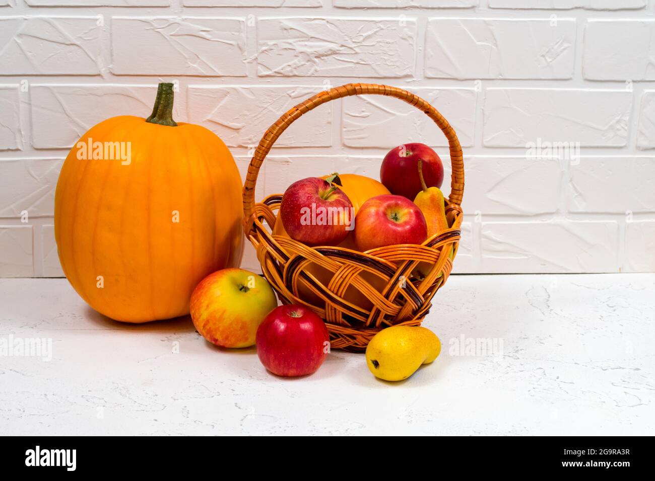 Orangefarbene Kürbisse mit Äpfeln und Birnen in einem Weidenkorb auf weißem Hintergrund. Stillleben im Herbst. Stockfoto