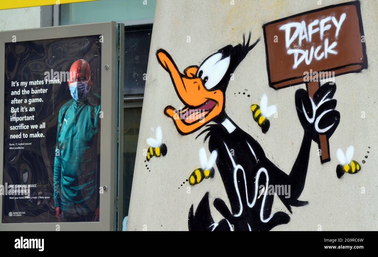 Bild der Zeichentrickfigur Daffy Duck, Teil eines Looney Tunes Kunstpfades, der in Manchester, England, eröffnet wurde, neben einem Covid-Gesundheitsposter Stockfoto