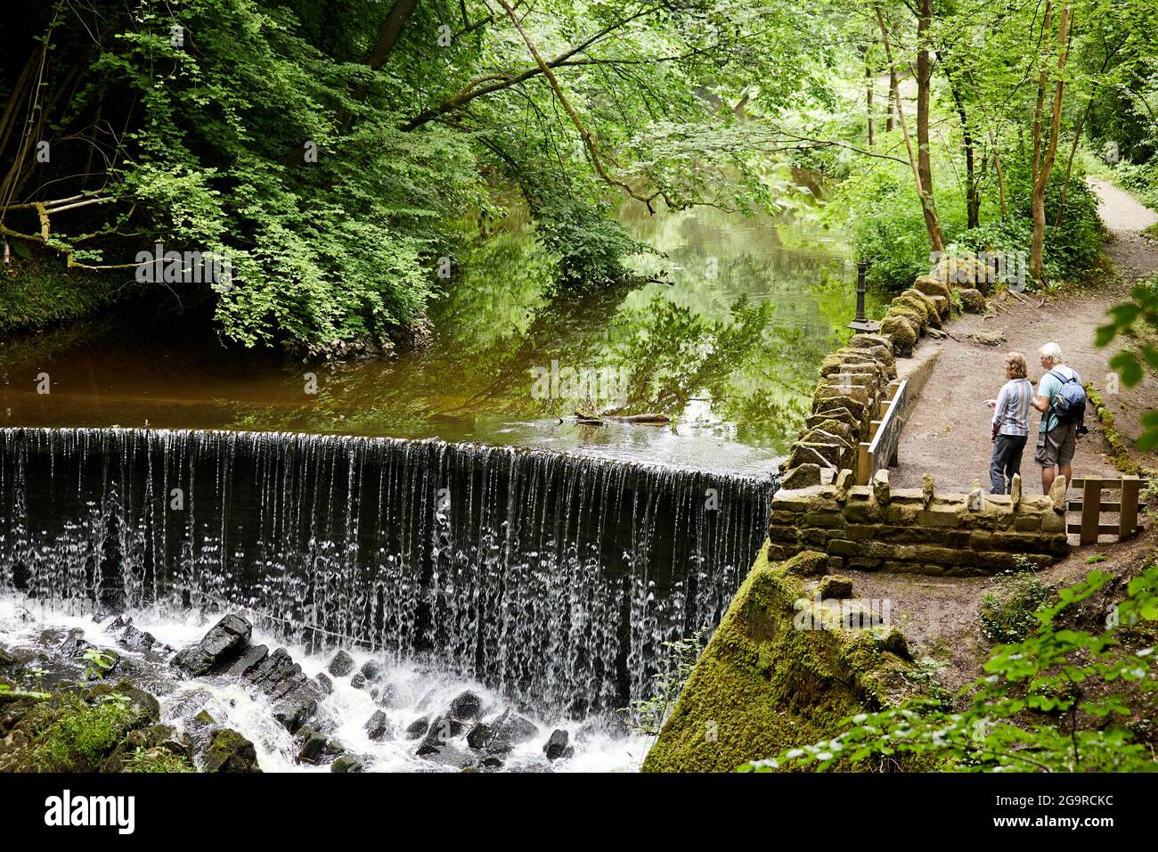 Ein älteres Paar, das bei einem Wasserfall während ihres Spaziergangs in Skipton Castle Woods steht Stockfoto