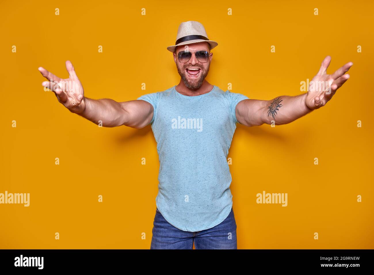 Kommt näher, lasst mich Euch umarmen. Studioaufnahme eines positiv freundlichen bärtigen Mannes in trendigem Outfit und Hut, der die Hände zur Kamera zieht und seine Freunde dazu einlädt Stockfoto