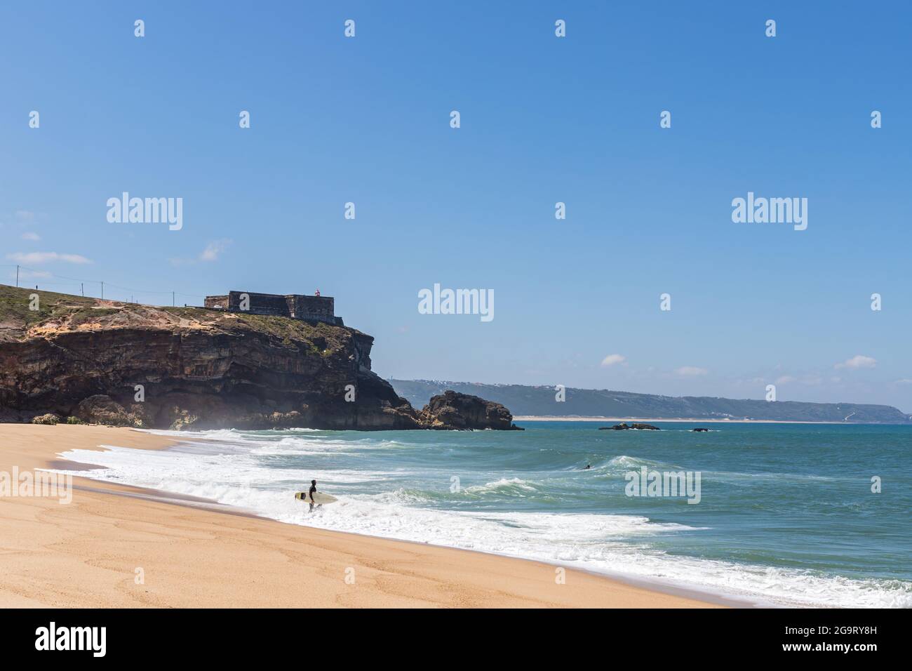 Nazare, Portugal - 29. Juni 2021: Ein Surfer am North Beach spaziert unterhalb der Festung Nazare ins Meer Stockfoto