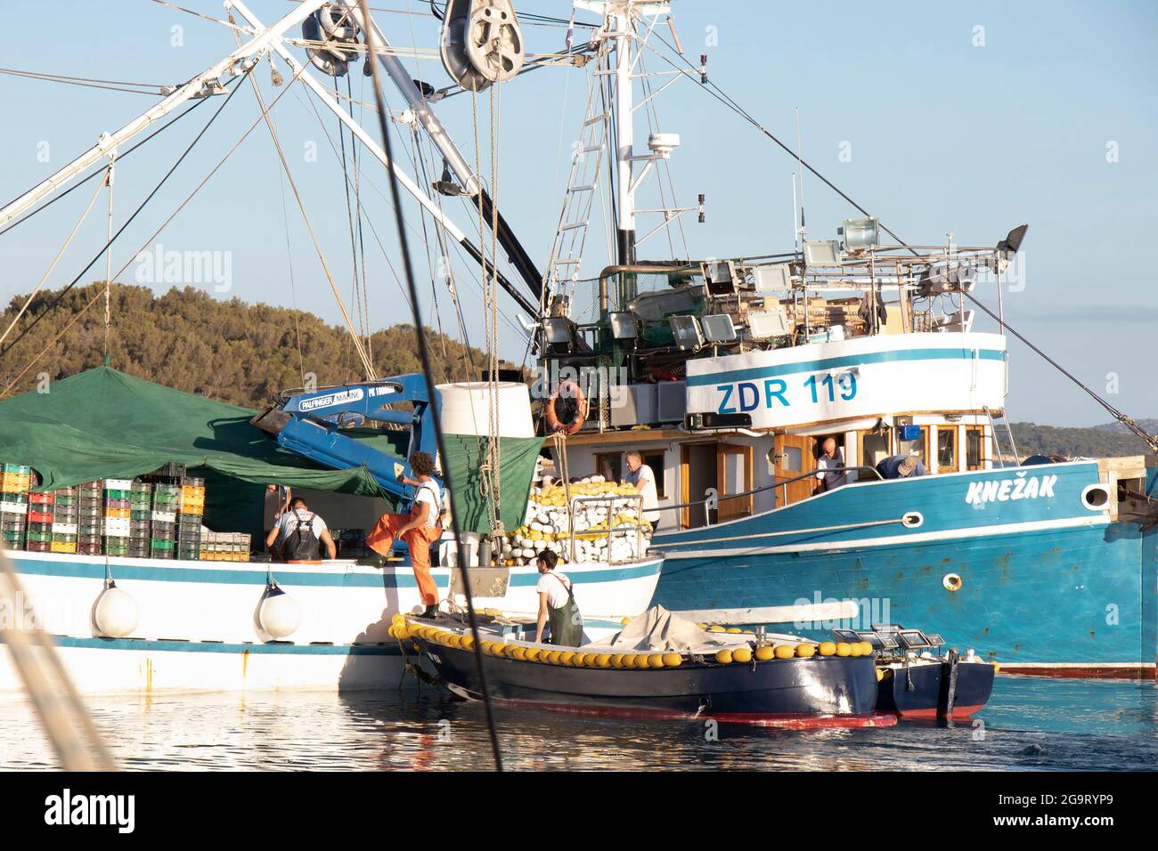 Tribunj, Kroatien - 1. Juli 2021: Fischer, die von einem kleinen Boot aus auf ein Fischerschiff steigen, am Sommertag am Hafen Stockfoto