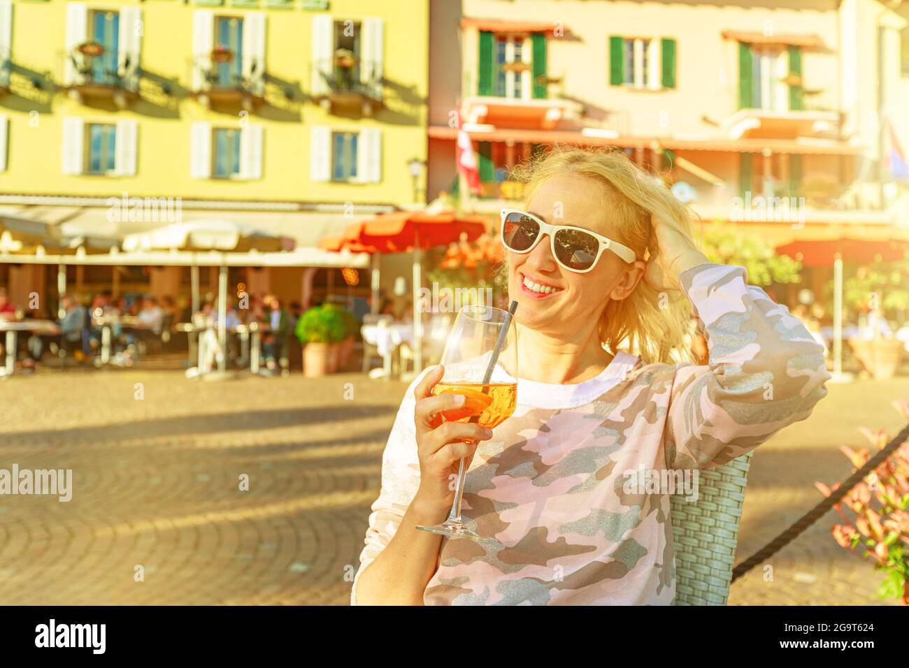 Tourist trinkt bei Sonnenuntergang einen Cocktail am Seeufer in einem Straßenlokal der Stadt Ascona in der Schweiz, im Kanton Tessin am Langensee. Stockfoto