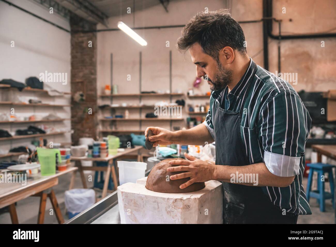 Erwachsener hispanischer Mann, der in einer Werkstatt einen Tontopf auf einem Tisch macht Stockfoto