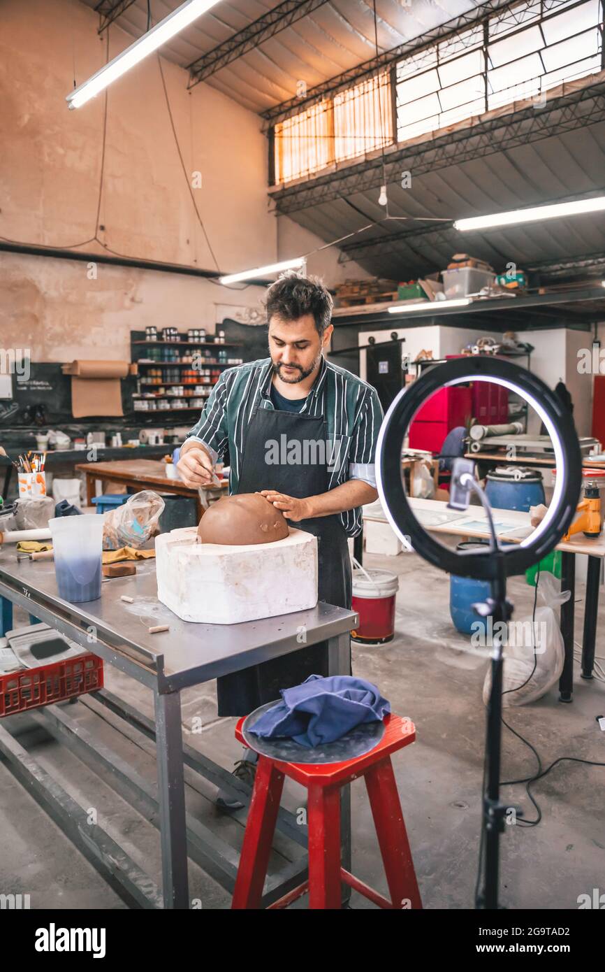 Erwachsener hispanischer Mann, der in einer Werkstatt einen Tontopf auf einem Tisch macht Stockfoto