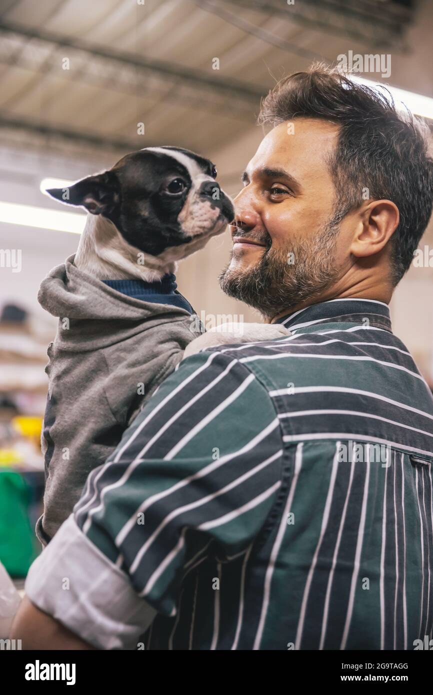 Porträt eines erwachsenen hispanischen Mannes, der eine französische Bulldogge mit einer Jacke in der Hand hält Stockfoto