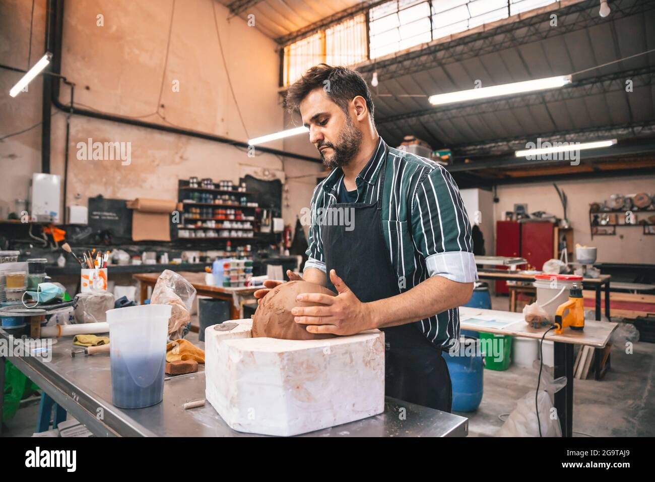 Erwachsener hispanischer Mann, der in einer Werkstatt einen Tontopf auf einem Tisch macht Stockfoto