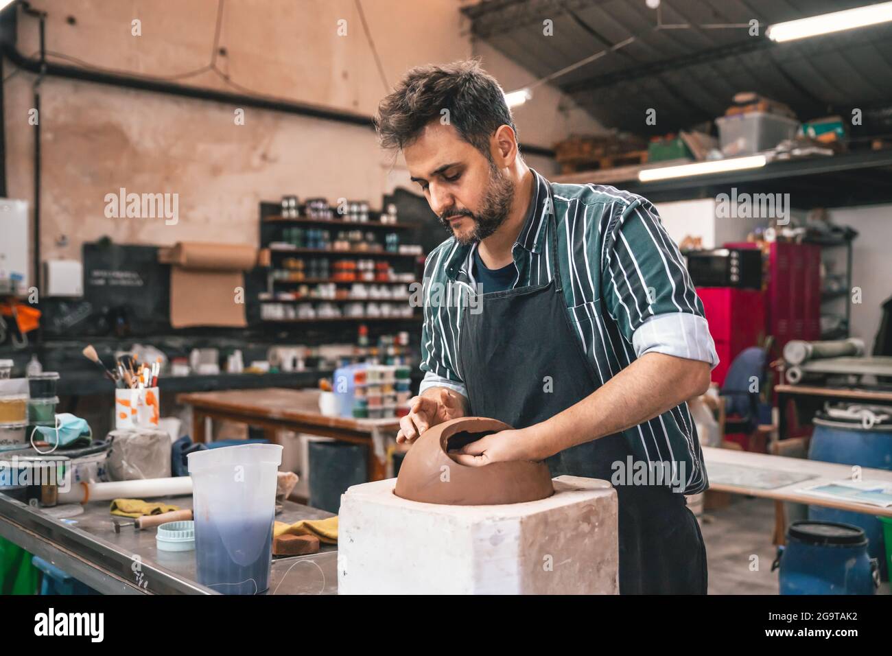 Erwachsener hispanischer Mann, der in einer Werkstatt einen Tontopf auf einem Tisch macht Stockfoto