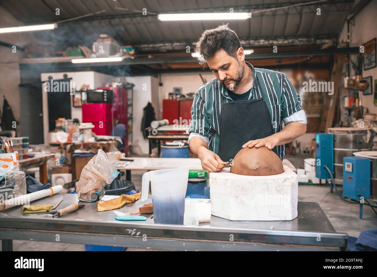 Erwachsener hispanischer Mann, der in einer Werkstatt einen Tontopf auf einem Tisch macht Stockfoto