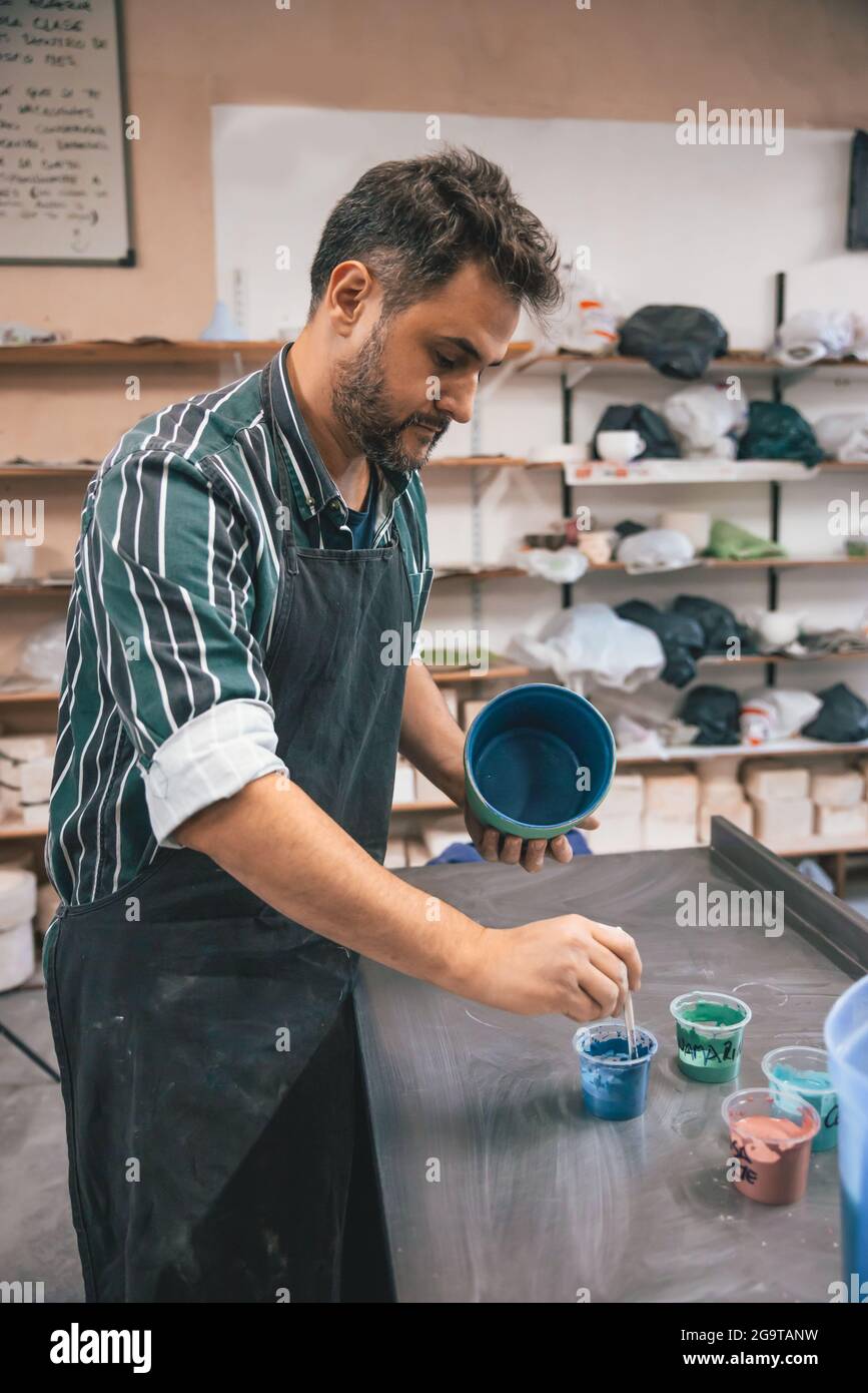Ein erwachsener hispanischer Mann malte in einer Werkstatt mit verschwommenem Hintergrund einen Tontopf Stockfoto