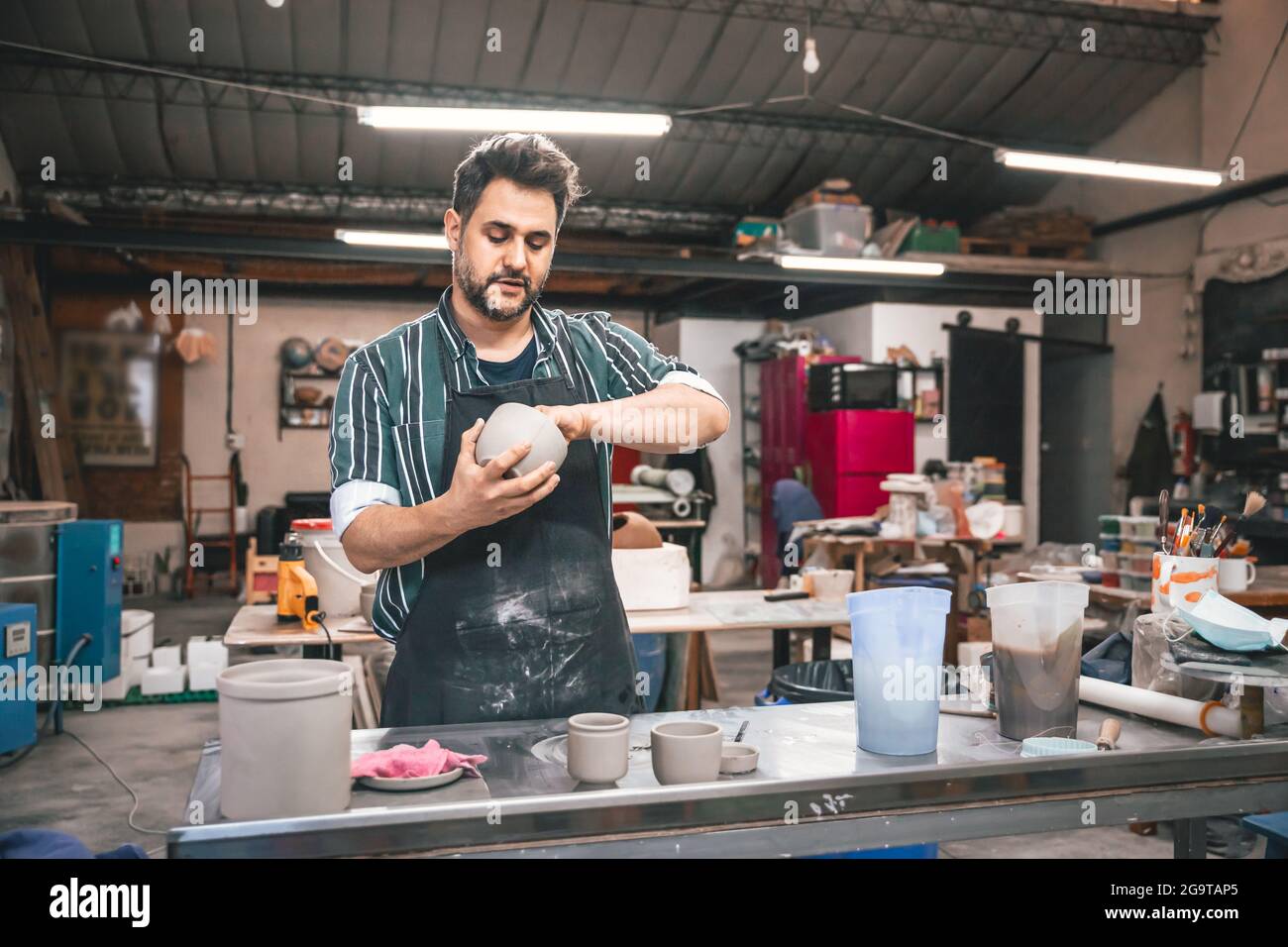 Erwachsener hispanischer Mann, der in einer Werkstatt einen Tontopf über einem Tisch macht Stockfoto