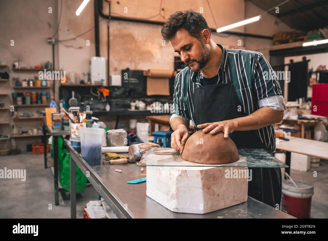 Erwachsener hispanischer Mann, der in einer Werkstatt einen Tontopf auf einem Tisch macht Stockfoto