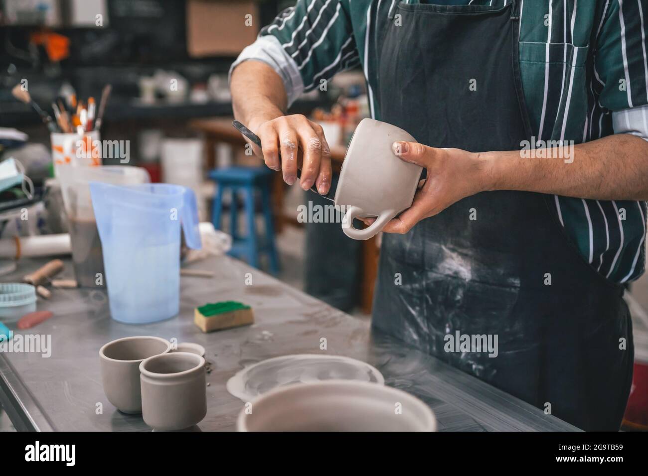 Erwachsener Mann, der in einer Werkstatt einen Tontopf über einem Tisch schnitzt Stockfoto