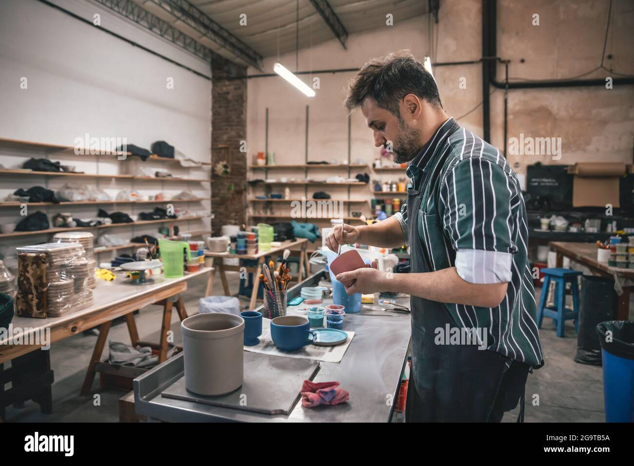 Ein erwachsener hispanischer Mann schnitzt in einer Werkstatt einen Tontopf über einem Tisch Stockfoto