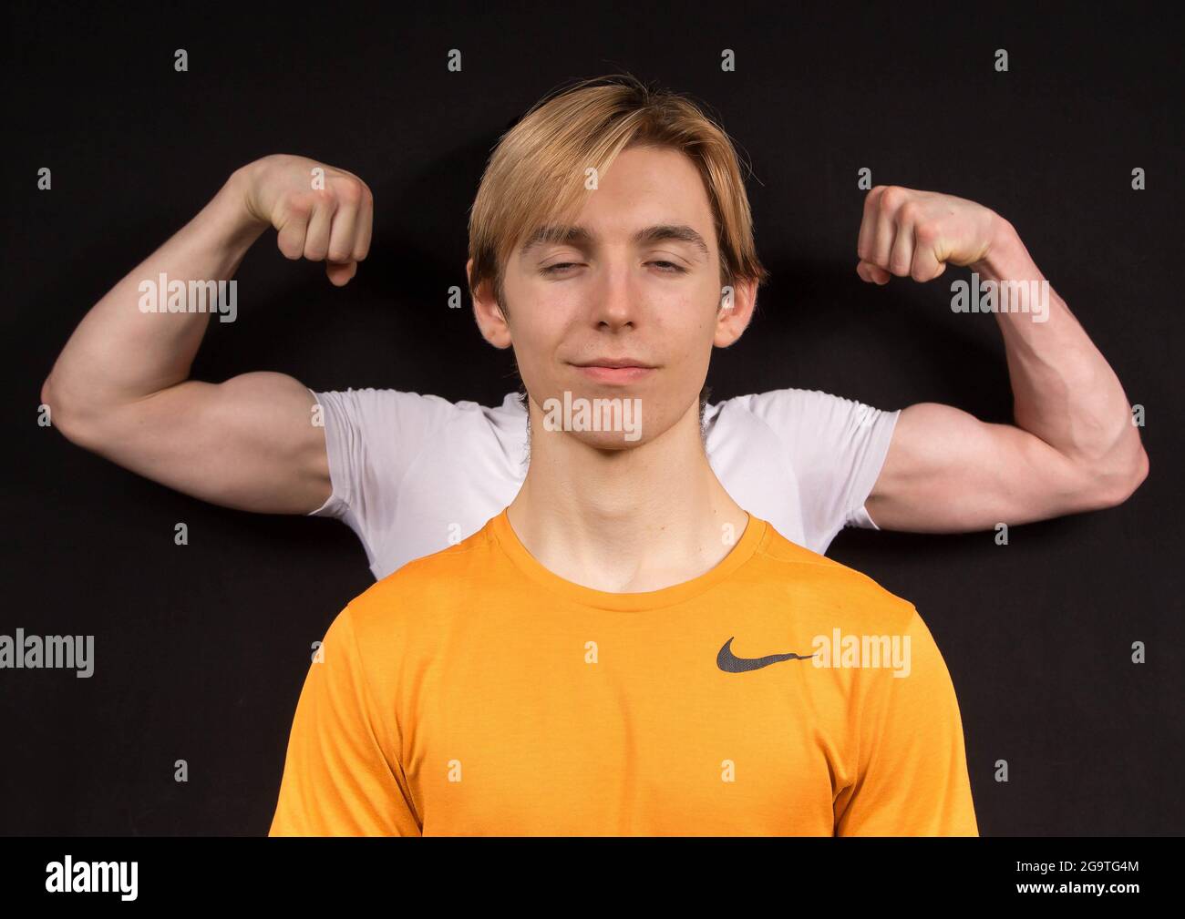 Ein männlicher Jugendlicher träumt davon, große muskulöse Arme zu haben, während ein anderer Jugendlicher seinen Bizeps hinter sich beugt Stockfoto