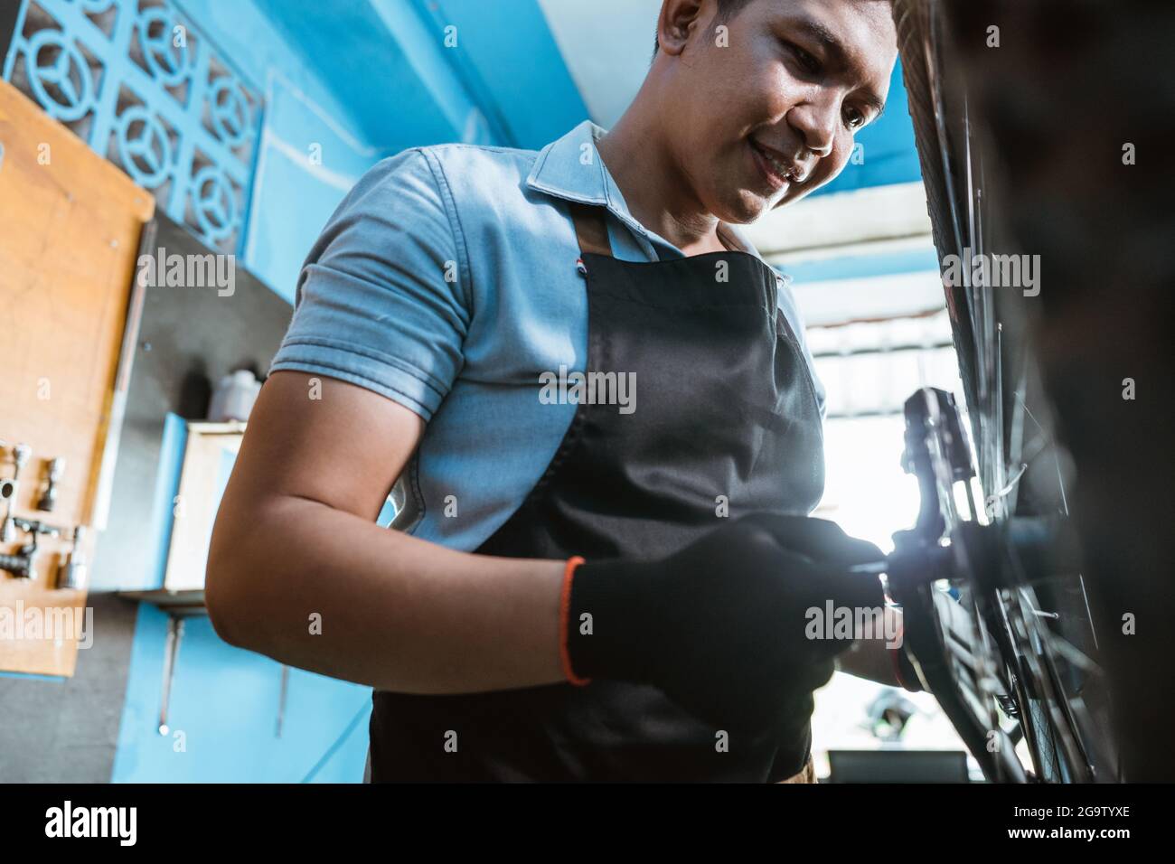Nahaufnahme eines Fahrradmechanikers in Schürze und Handschuhe, die Achsen einbauen Stockfoto