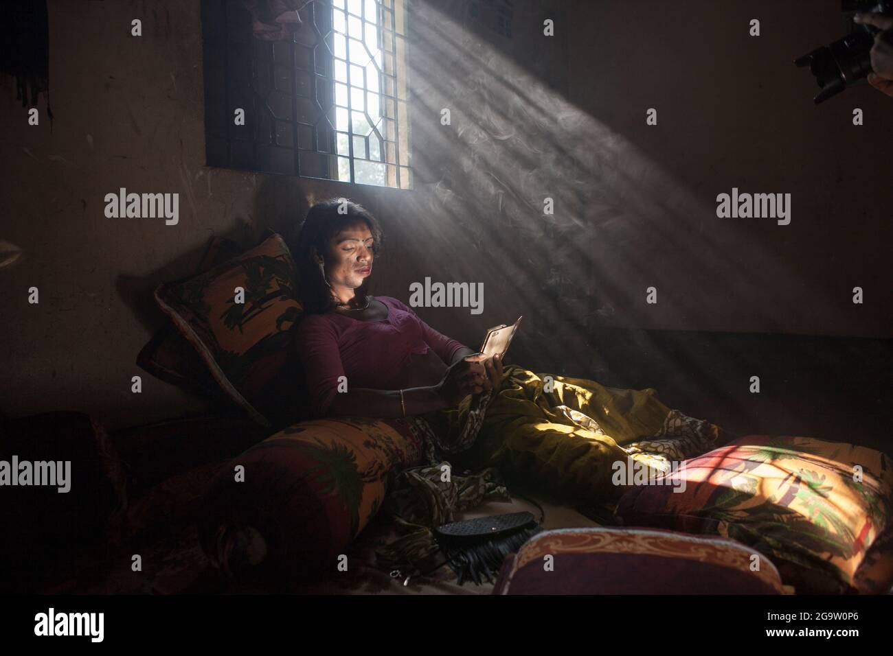 Transgender-Frau in Indien, die ein Smartphone in ihrem Zimmer benutzt, in natürlichem Licht von einem Fenster gebadet, symbolisiert Verbindung, Identität und Widerstandsfähigkeit Stockfoto