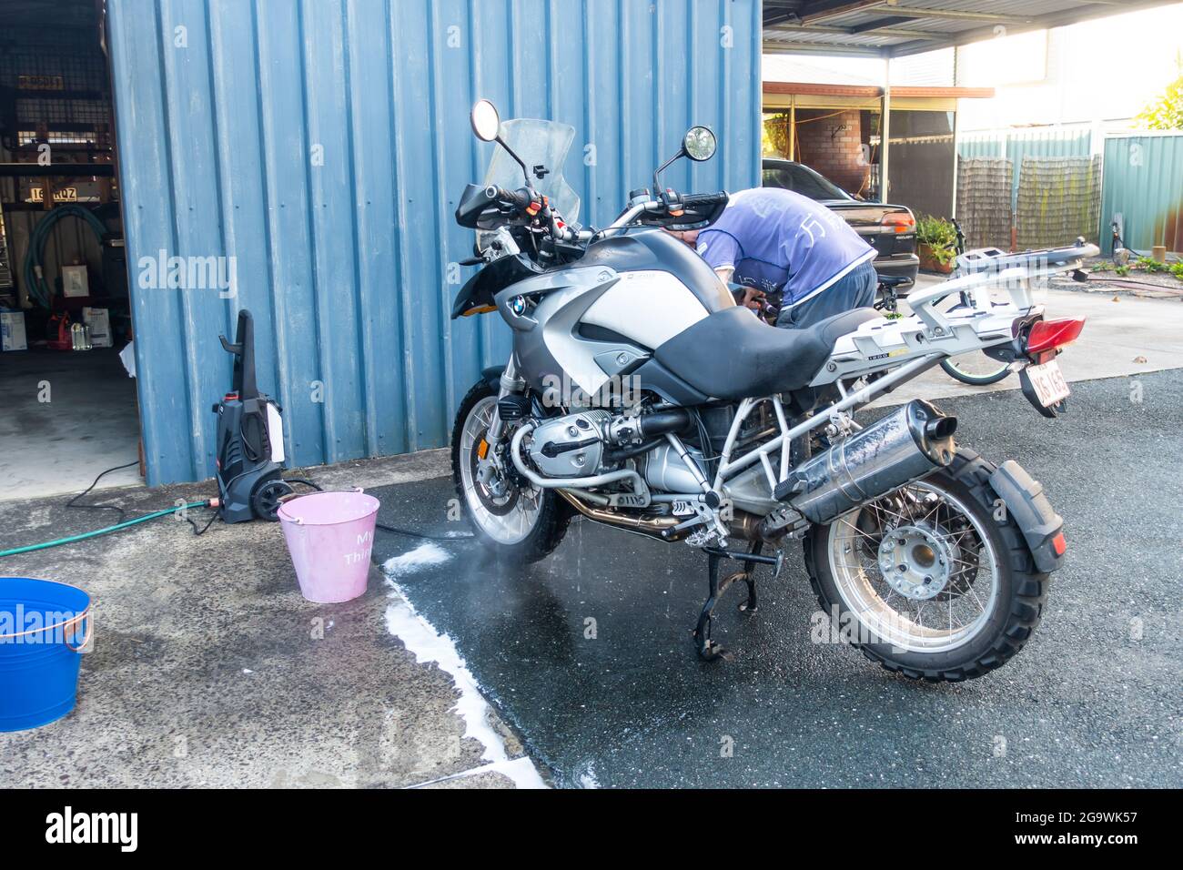 Mann wäscht sein BMW R1200 GS Motorrad mit Hochdruckwasserschlauch. Stockfoto