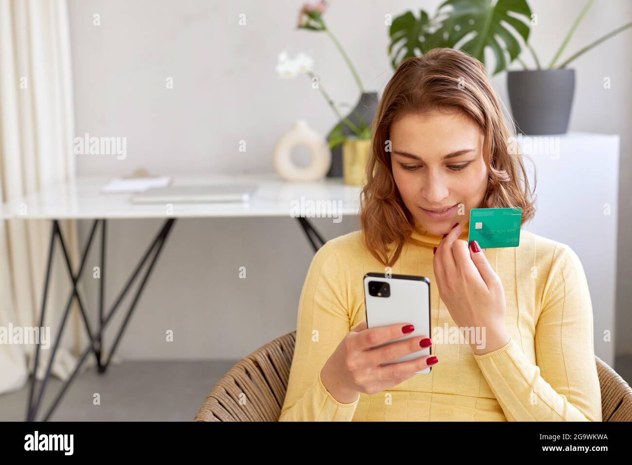 Entzückte Frau mit Plastikkarte und Smartphone macht Online-Kauf zu Hause. Lächelnde Frau, die per Karte für den Online-Kauf per Telefon bezahlt Stockfoto