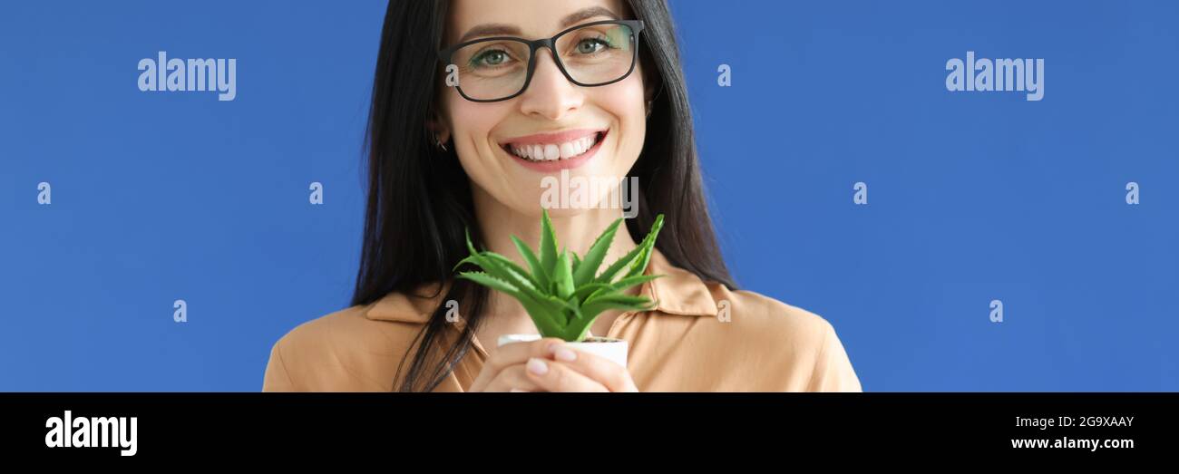 Frau mit Brille, die den Blumentopf in den Händen auf Blau hält Hintergrund Stockfoto