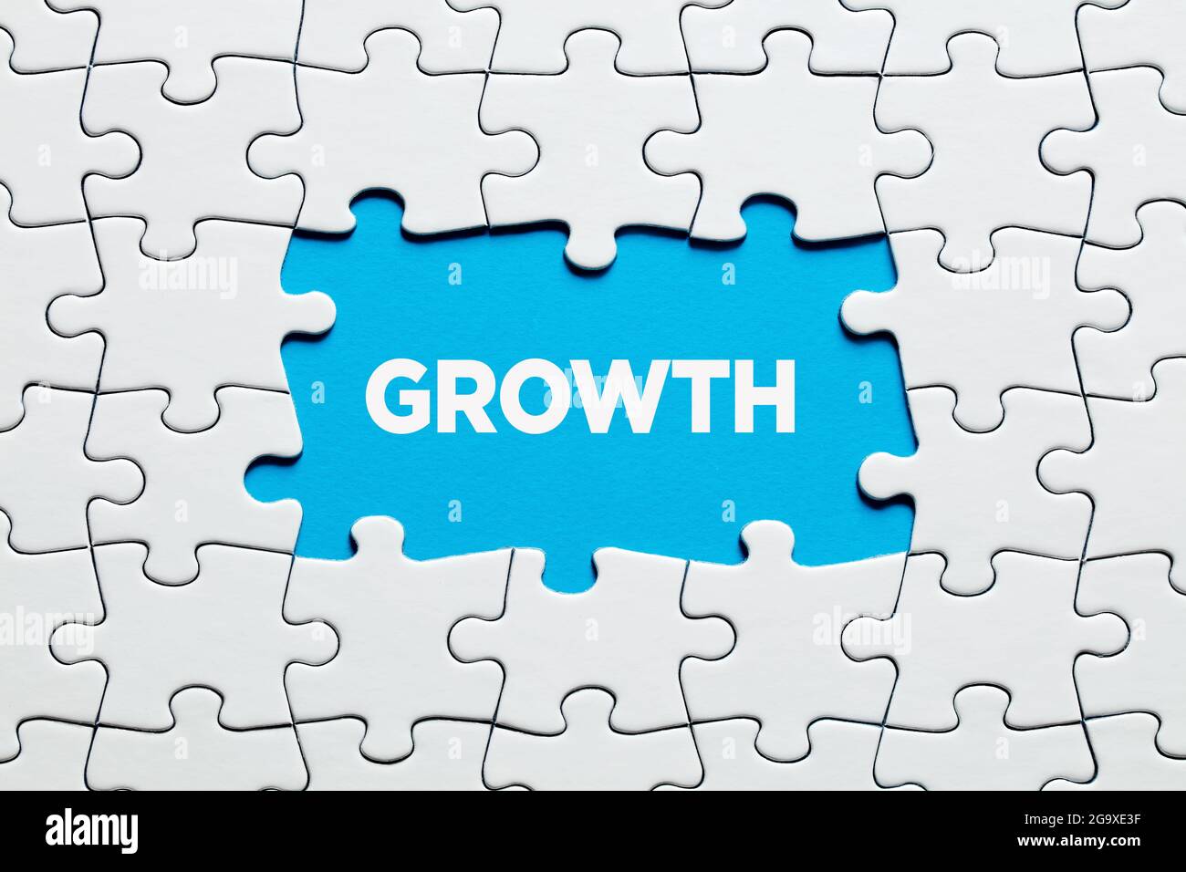 Das Wort Wachstum auf blauem Hintergrund Fragment von weißen Puzzle umgeben. Geschäftliches, finanzielles oder persönliches Wachstum, Verbesserung oder Entwicklung. Stockfoto