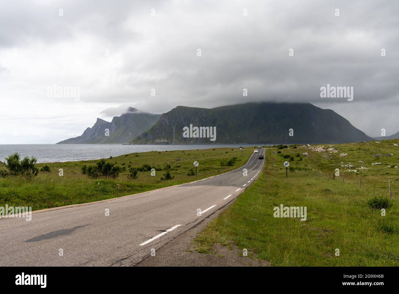 Flakstad, Norwegen - 20. Juli 2021: Küstenstraße auf den Lofoten-Inseln mit wenig Verkehr an einem bewölkten Tag Stockfoto