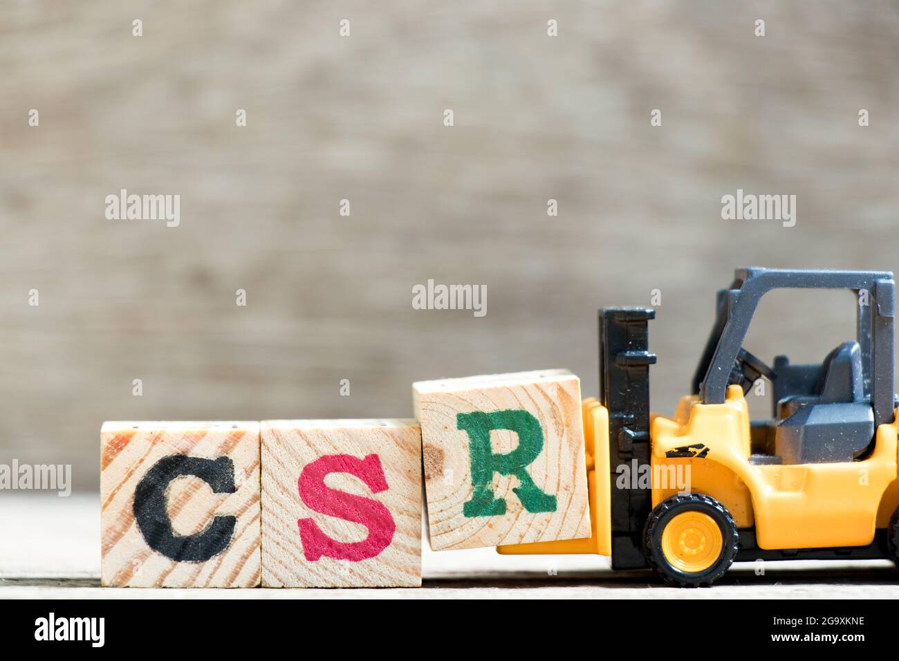 Spielzeug-Gabelstapler halten Buchstabenblock R in Wort CSR (Abkürzung von Corporate Social Responsibility) auf Holz Hintergrund Stockfoto