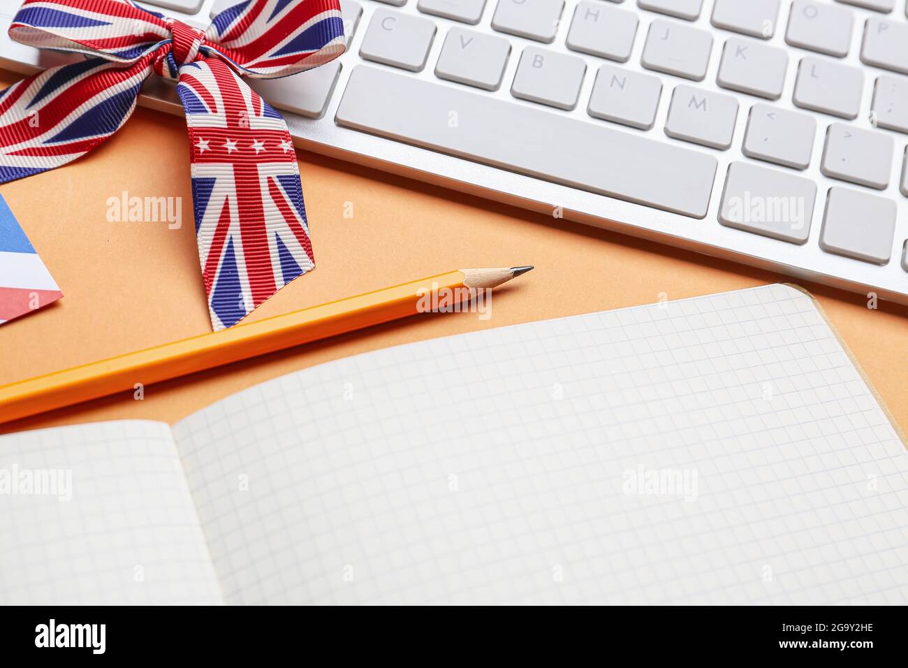 Schreibwaren, Tastatur und Band in den Farben der britischen Flagge auf orangefarbenem Hintergrund. Konzept des Englischlernens Stockfoto