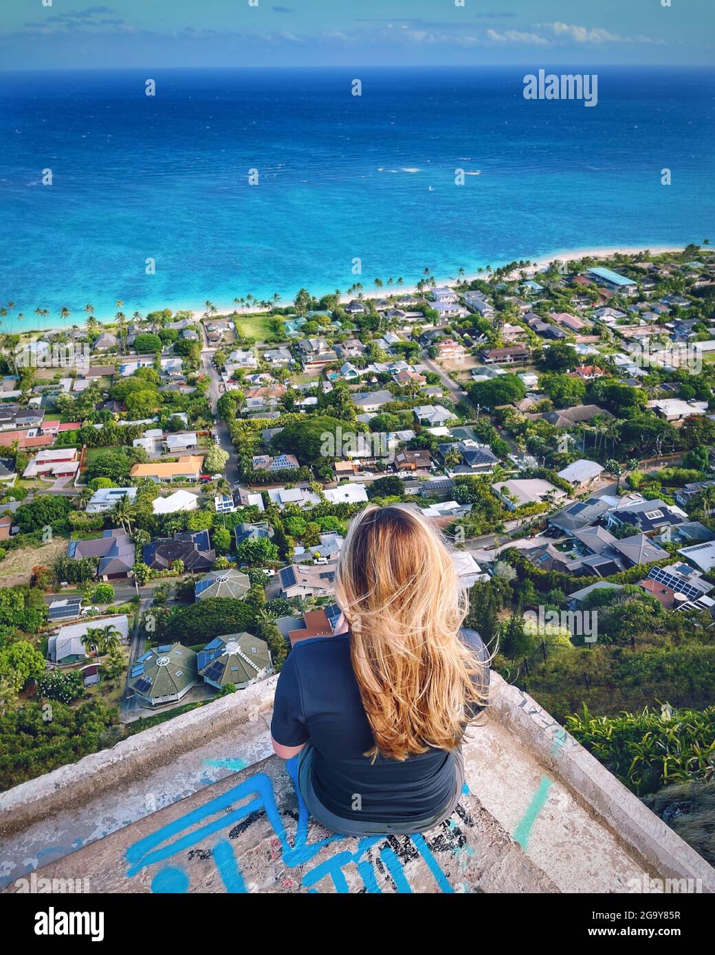 Rückansicht einer Frau, die auf einem Bunker sitzt und die Kailua Bay, Oahu, Hawaii, USA, betrachtet Stockfoto