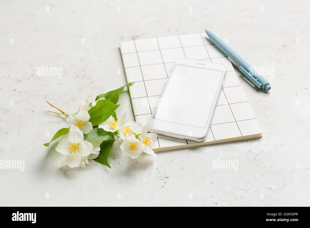 Handy, Notizbuch, Stift und Jasminblüten auf hellem Hintergrund Stockfoto