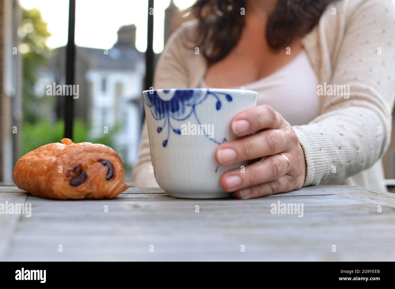 Frau genießt eine Tasse Kaffee und ein Pain au Chocolate Gebäck Stockfoto