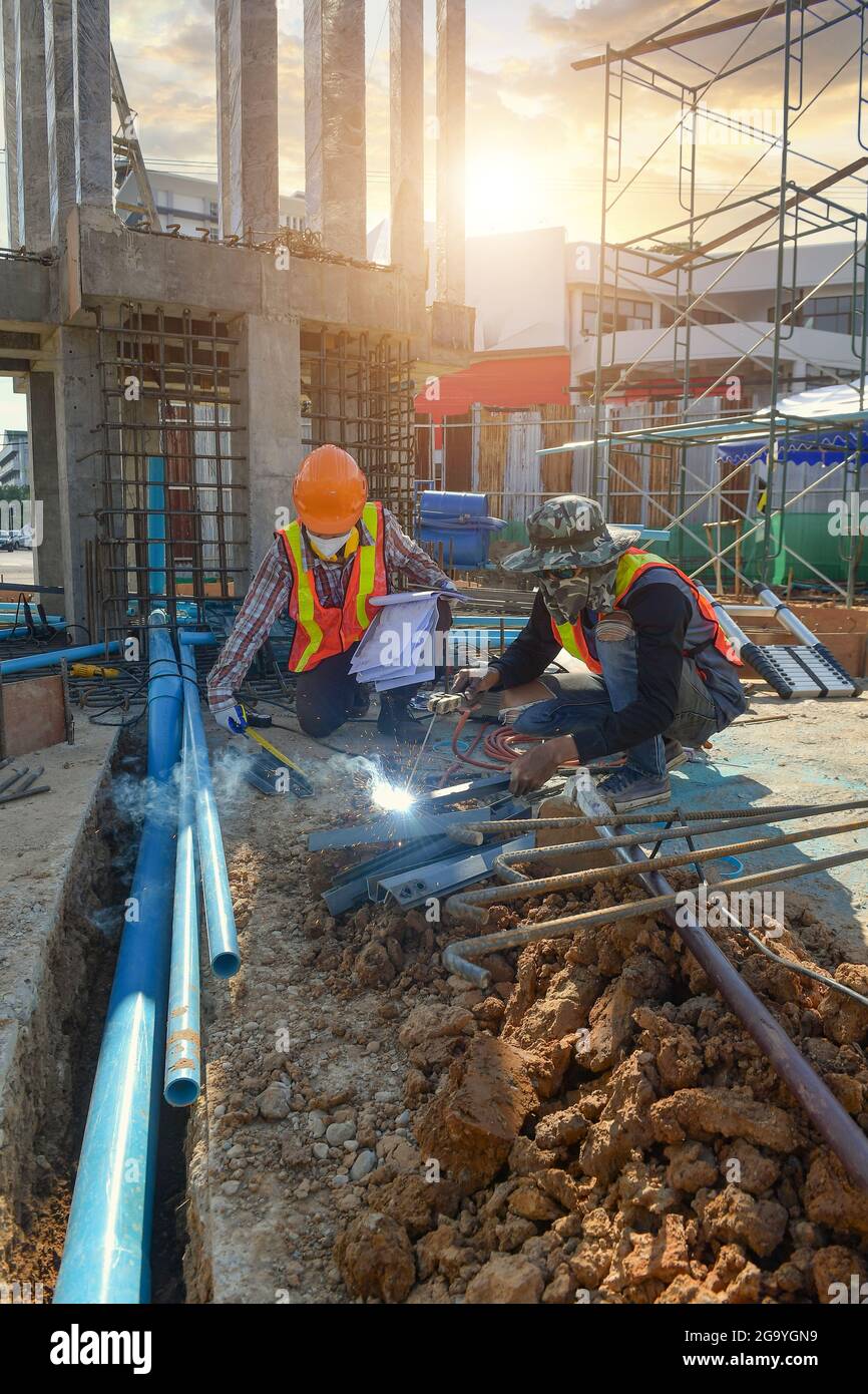 Vorarbeiter auf einer Baustelle, die ein Metallstück misst, und ein Arbeiter, der ein Metallstück schweißen muss, Thailand Stockfoto