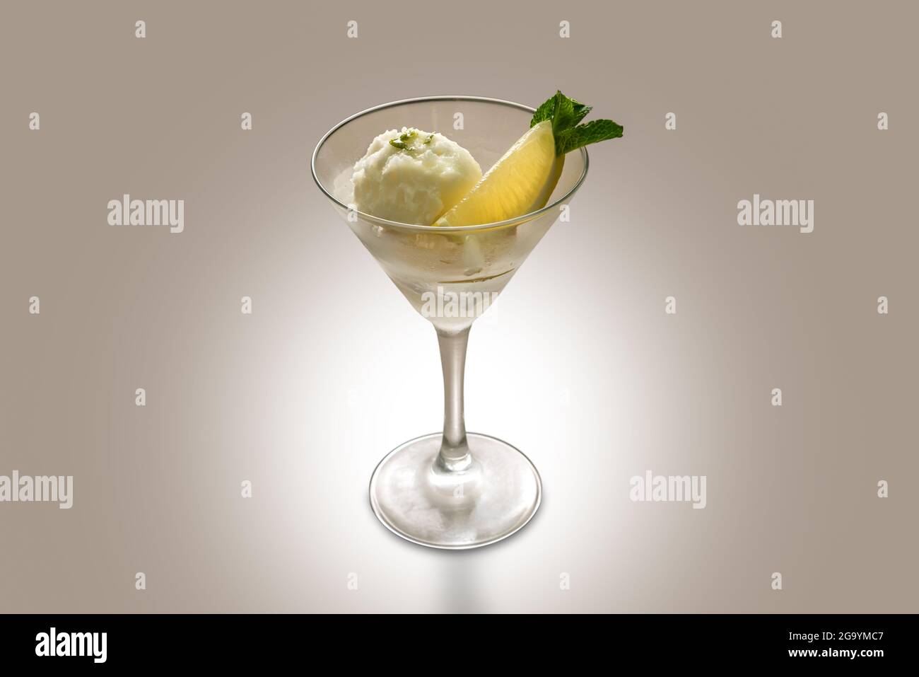 Zitronensorbet mit Zitronenscheibe und Minzblättern in martiniglas auf hellbraunem Hintergrund, Kopierfläche Stockfoto