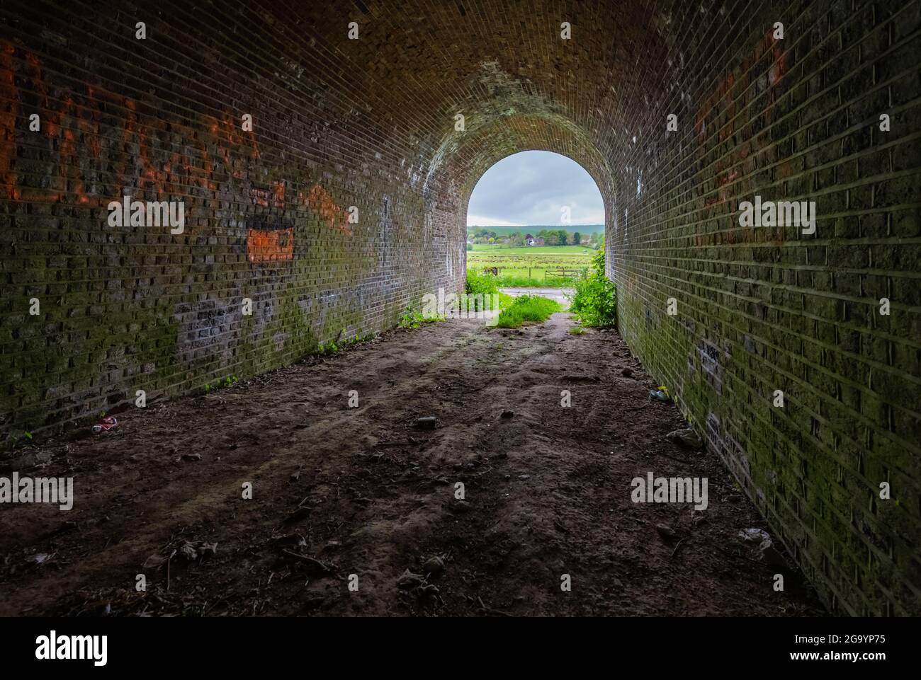 Im Inneren einer Backsteinbrücke unterstreichen sie die Eisenbahnbrücke, scheinbar ein Tunnel, der mit einem Weitwinkelobjektiv in Amberley, West Sussex, England, Großbritannien, auf den Ausgang blickt. Stockfoto