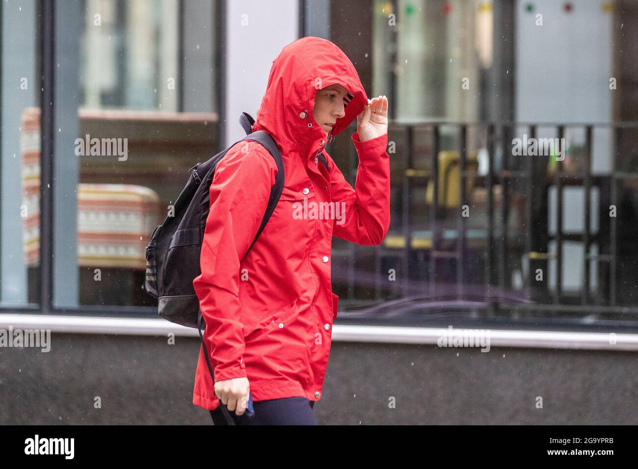 Frau in rotem Anorak mit Kapuze in Preston, Lancashire. UK Wetter 28. Juli 2021; Morgenregen im Stadtzentrum mit weiteren starken Schauern erwartet. Credit MediaWorldImages/AlamyLiveNews. Stockfoto