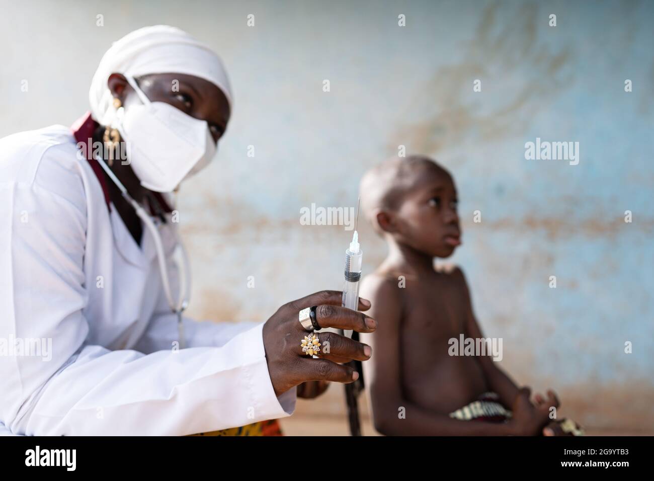 Auf diesem Bild spritzt eine junge afrikanische Krankenschwester mit einer schützenden Gesichtsmaske und einem weißen turbanähnlichen Schal um ihren Kopf Wasser von einer Spritze zum Pre Stockfoto