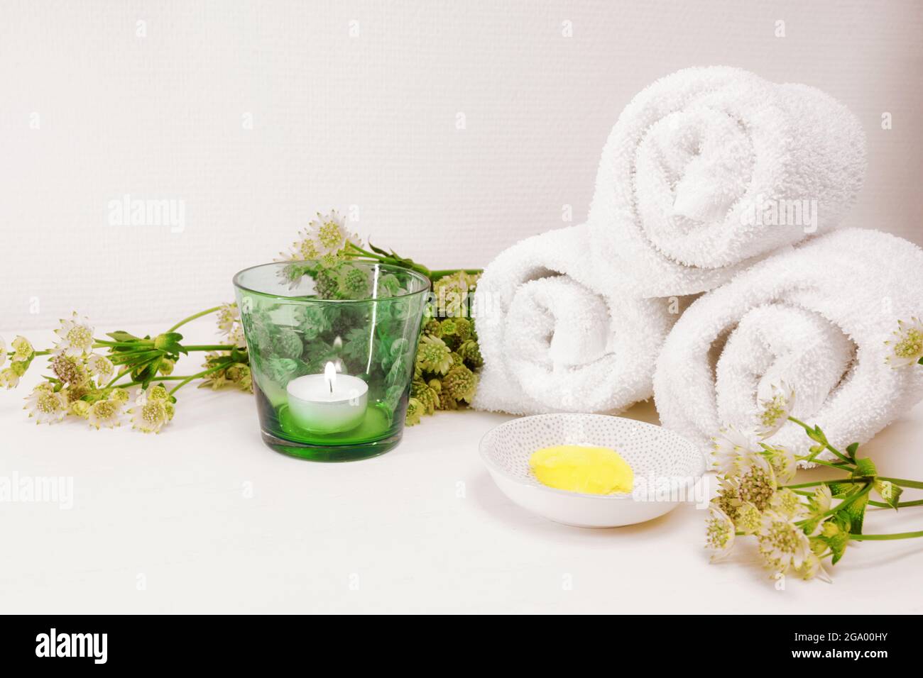 Kosmetische Feuchtigkeitscreme oder Weichmacher für Pediküre und weiche Fußhaut, weiße Handtücher, Kerze und einige grüne Blumen auf einem hellen Hintergrund mit großen Kopien Stockfoto