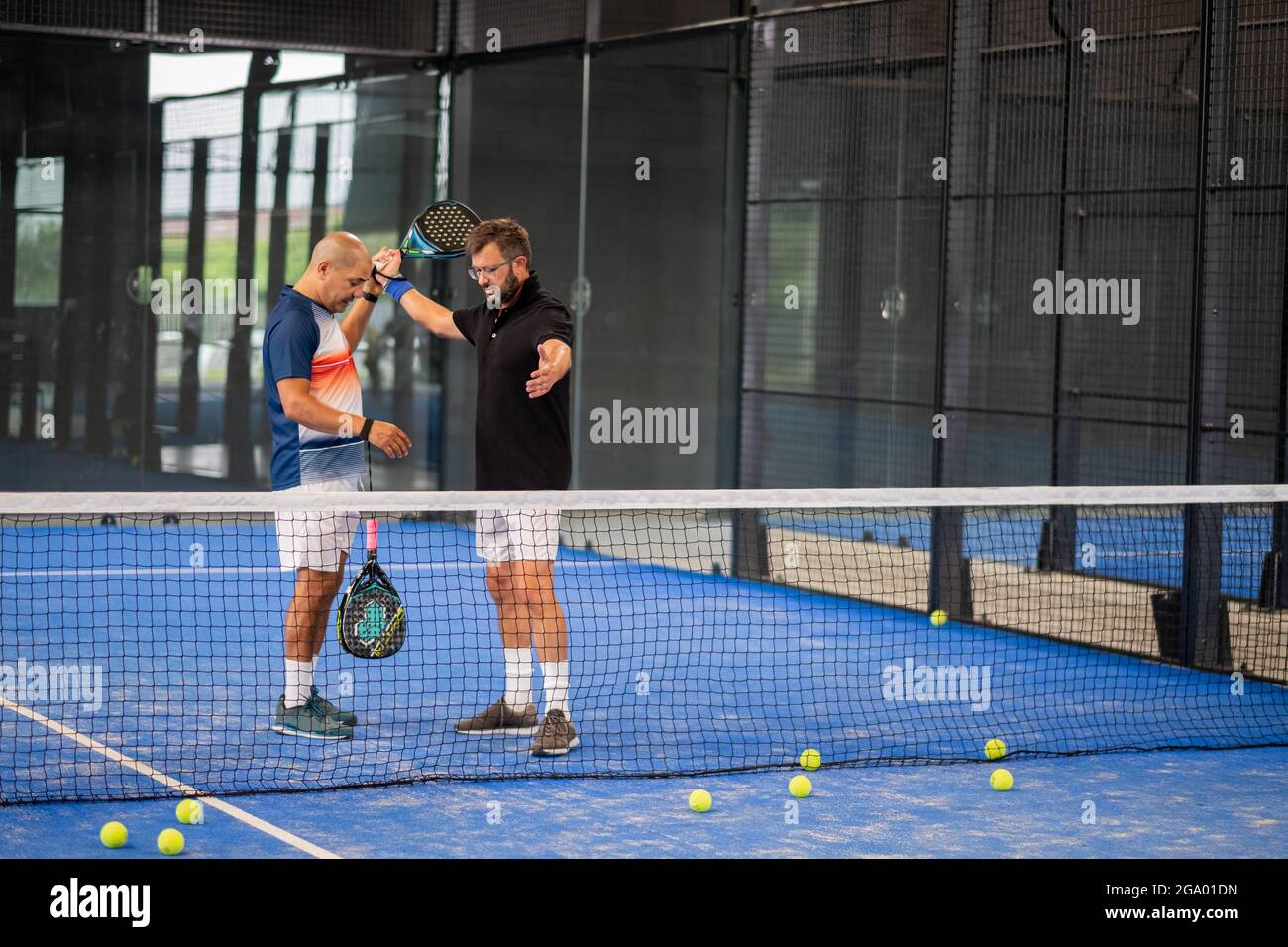 Überwachen Sie den Padel-Unterricht für den Mann, sein Schüler - Trainer lehrt Jungen, wie Padel auf dem Hallentennisplatz zu spielen Stockfoto