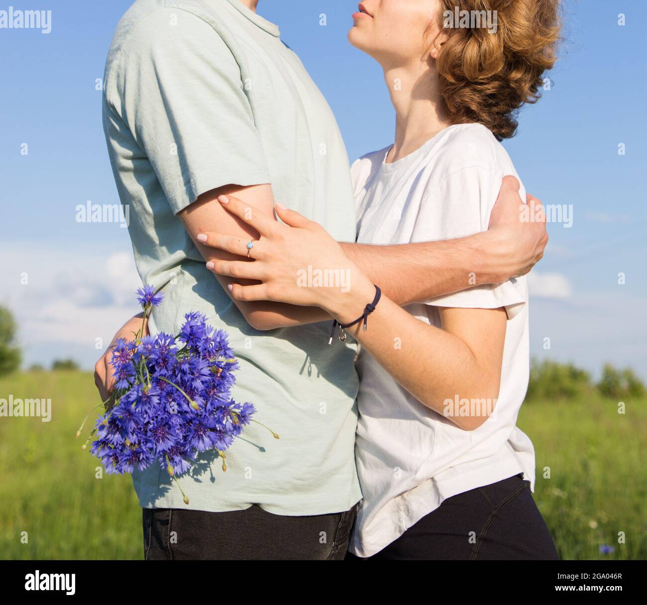 Unbekanntes junges Paar in der Liebe, Ruhe und Umarmung in der Natur an einem sonnigen Tag. Kleiner Junge und Mädchen mit einem Strauß Kornblumen. Zarte Gefühle, Romantik Stockfoto