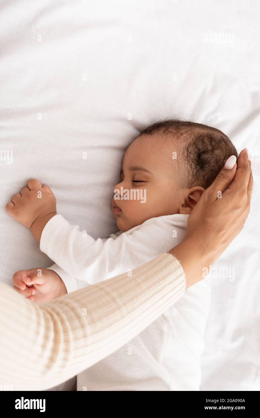 Schwarze Mutter streichelt mit der Hand und schläft den Kopf des Babys im Bett, abgeschnitten Stockfoto