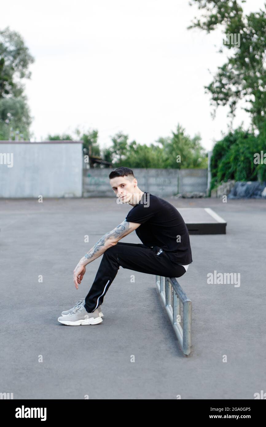Junge Brünette Mann sitzt allein auf einem Asphalt Skate Spielplatz Stockfoto