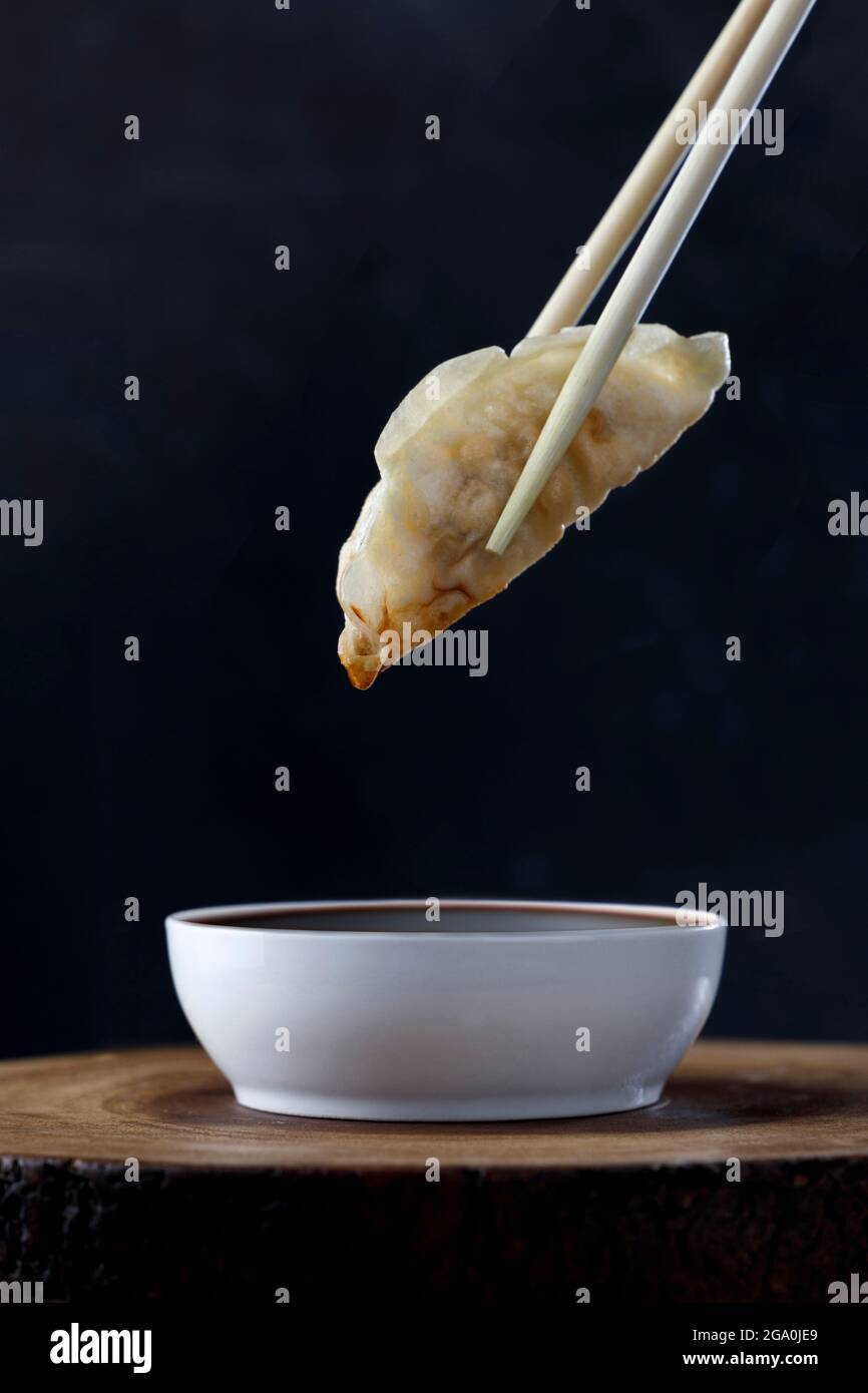 Chinesischer Knödel, der von Essstäbchen gehalten wird, die auf Soja mit schwarzem Hintergrund getaucht sind Stockfoto