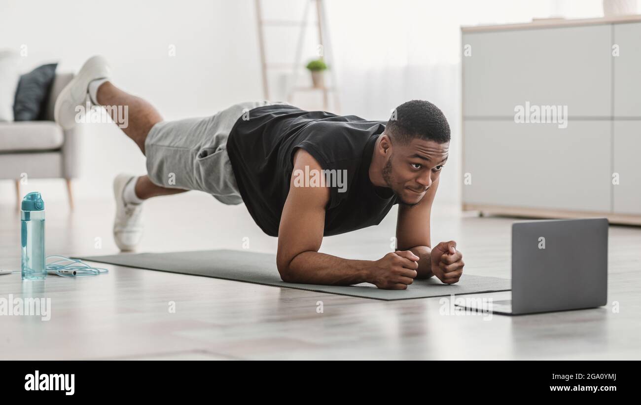 Mann Am Laptop, Der In Der Plank Steht Und Beinraise In Der Halle Macht Stockfoto